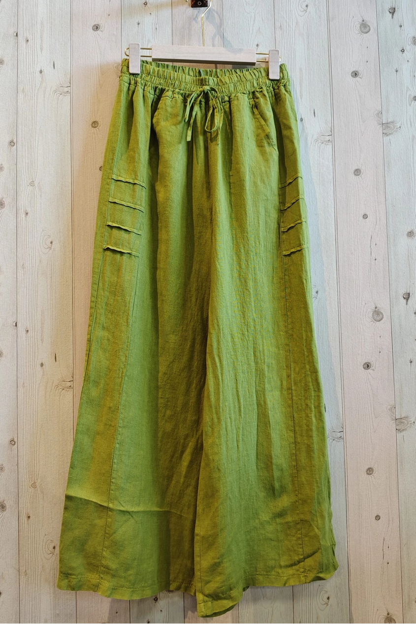 Green pants hanging on a wooden hanger against a wooden wall.