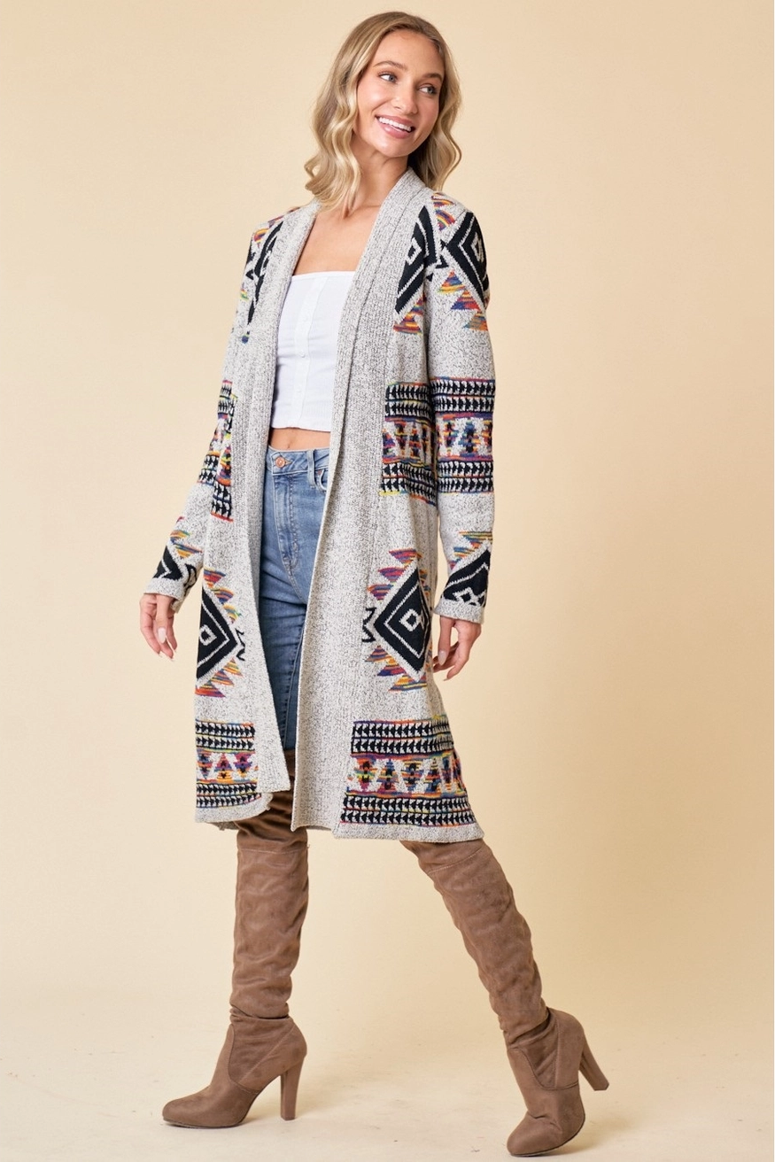 Woman wearing a patterned cardigan, white top, blue jeans, and brown boots on a beige background