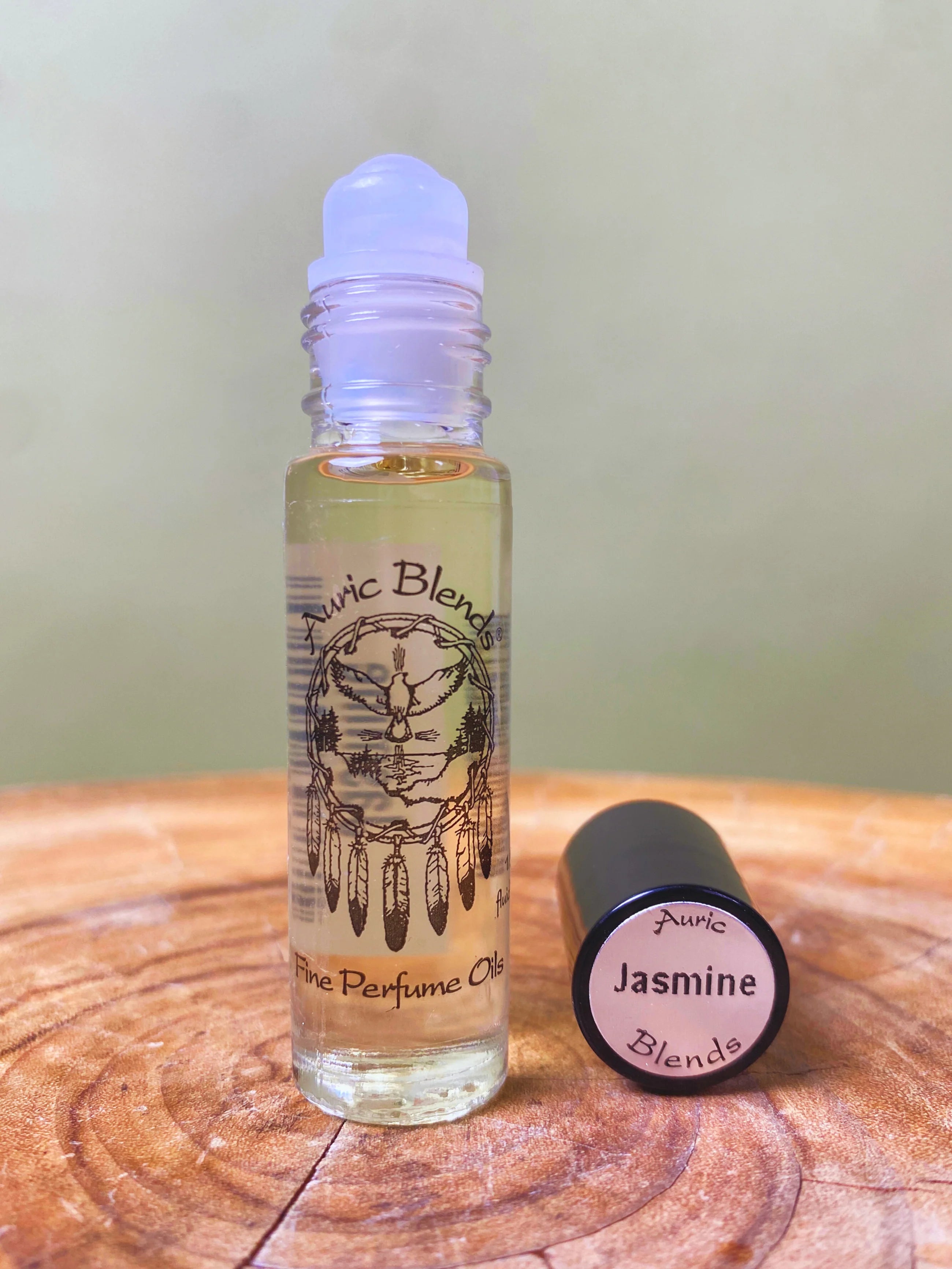 Roll-on bottle of Auric Blends perfume oil on a wooden surface with a green background