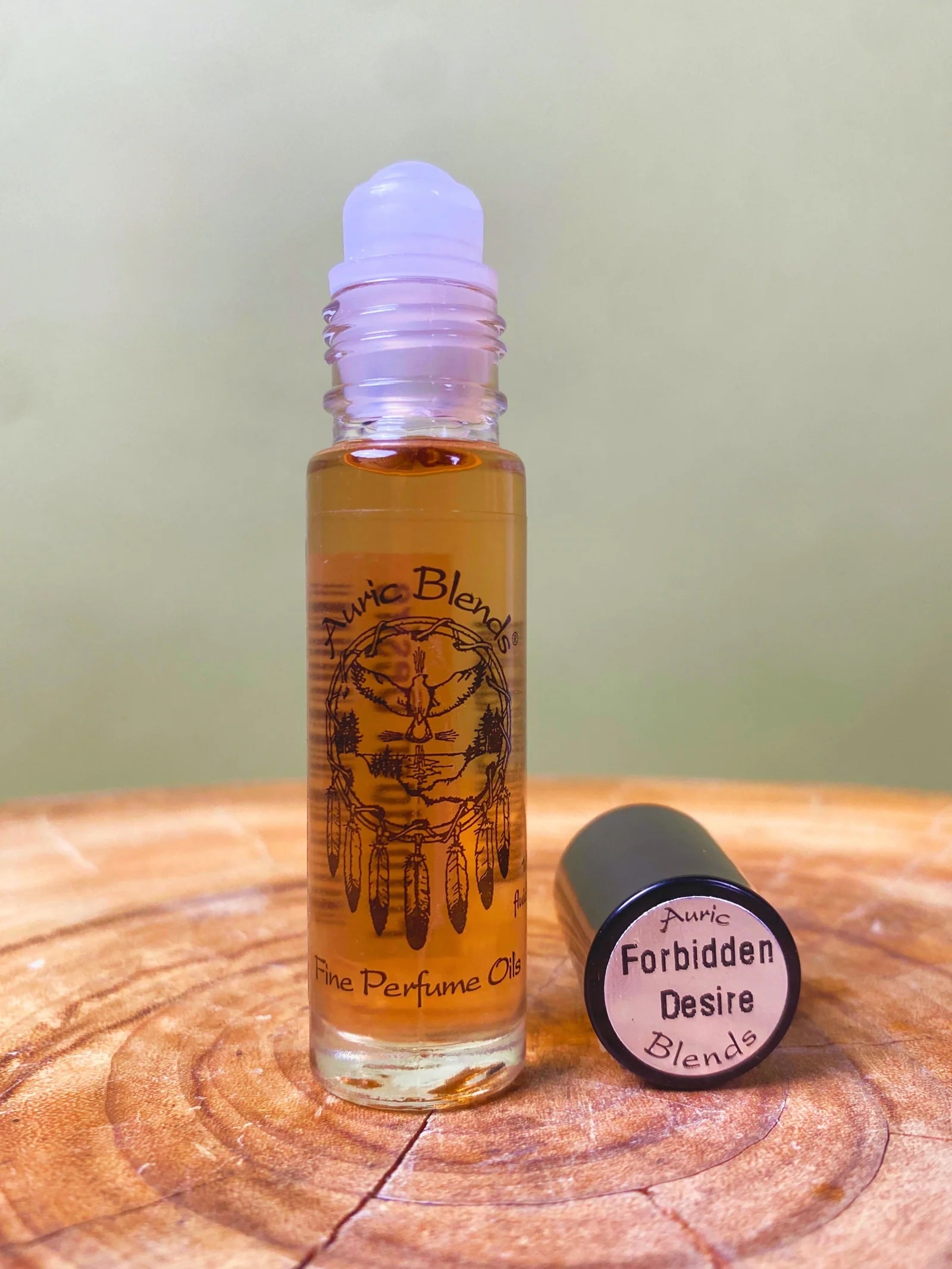 Roll-on bottle of perfume labeled 'Forbidden Desire Blends' on a wooden surface with a green background.