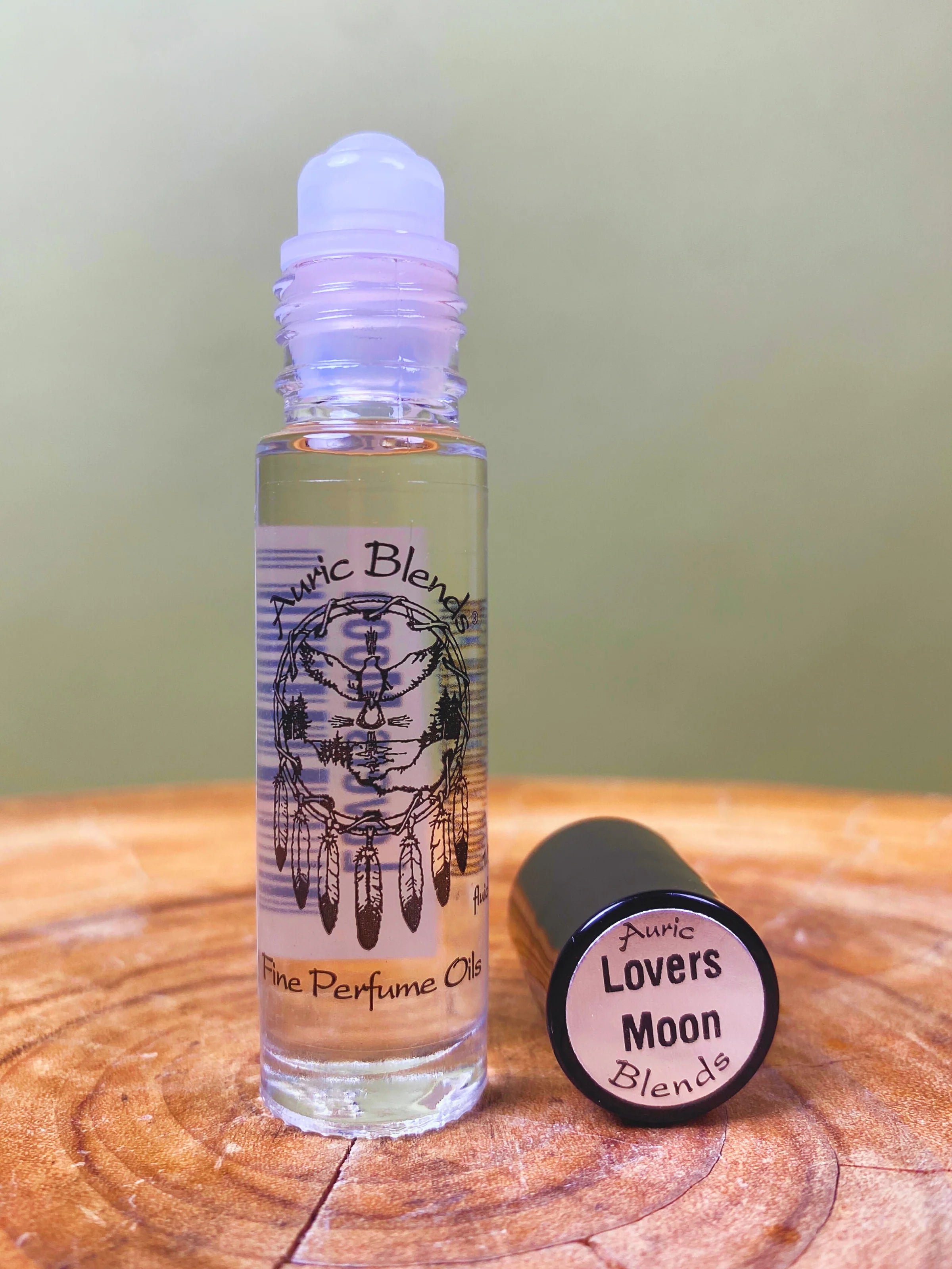 Roll-on perfume bottle labeled 'Auric Lovers Moon Blends' on a wooden surface with a green background.