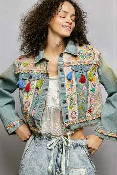 Woman wearing a colorful embroidered denim jacket on a gray background