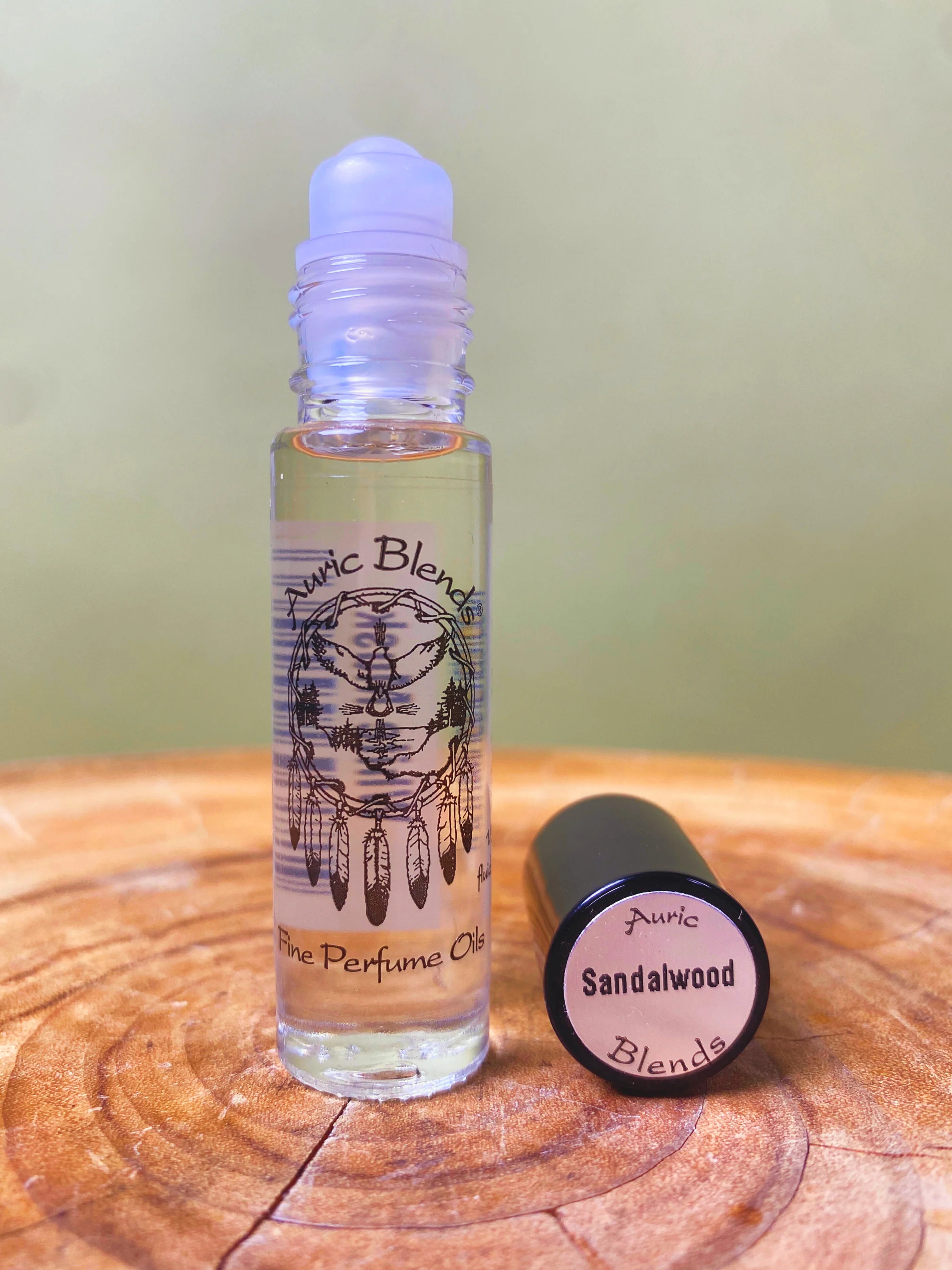 Roll-on bottle of Auric Blends Sandalwood perfume on a wooden surface with a green background