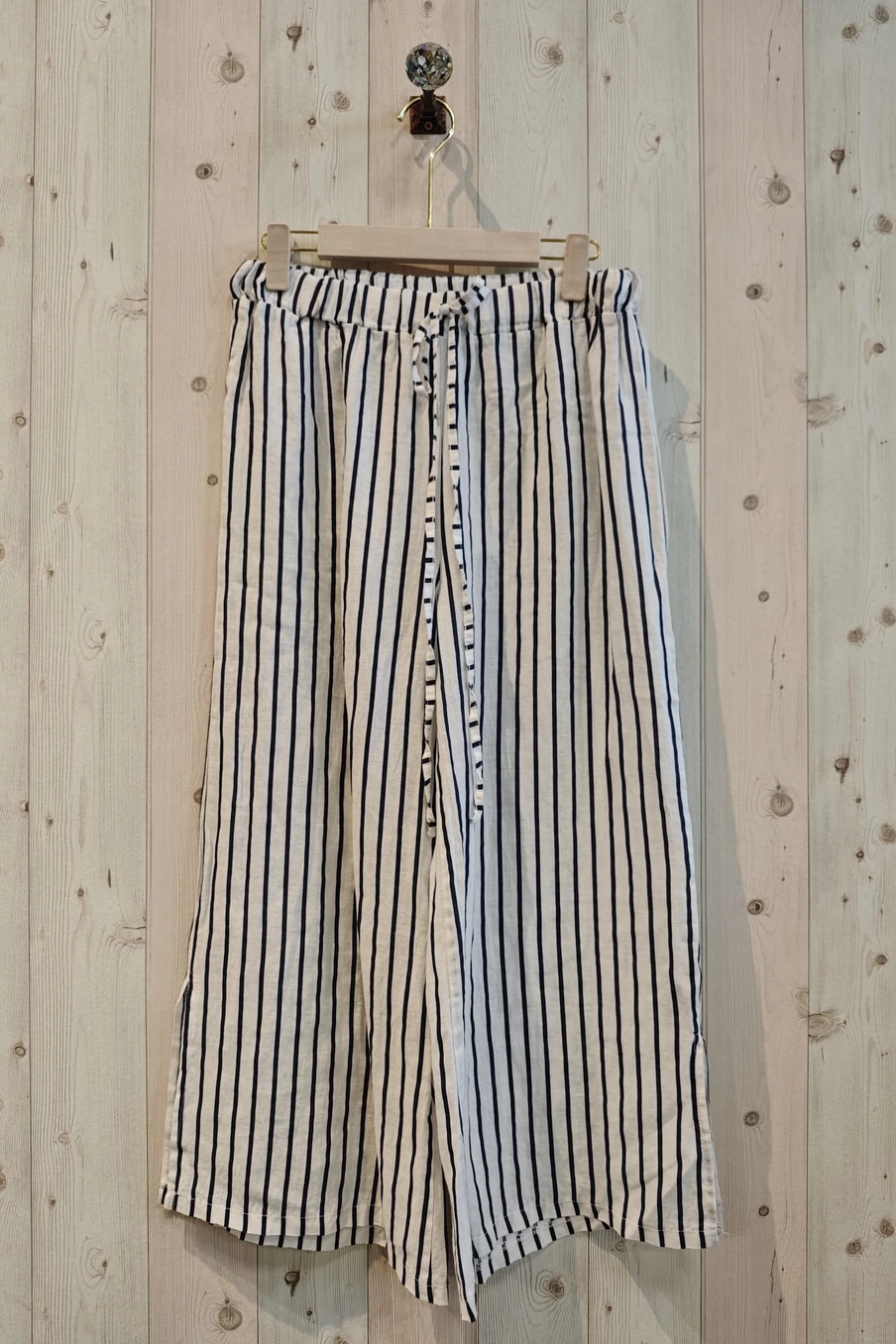 Striped pants hanging on a wooden hanger against a wooden wall.