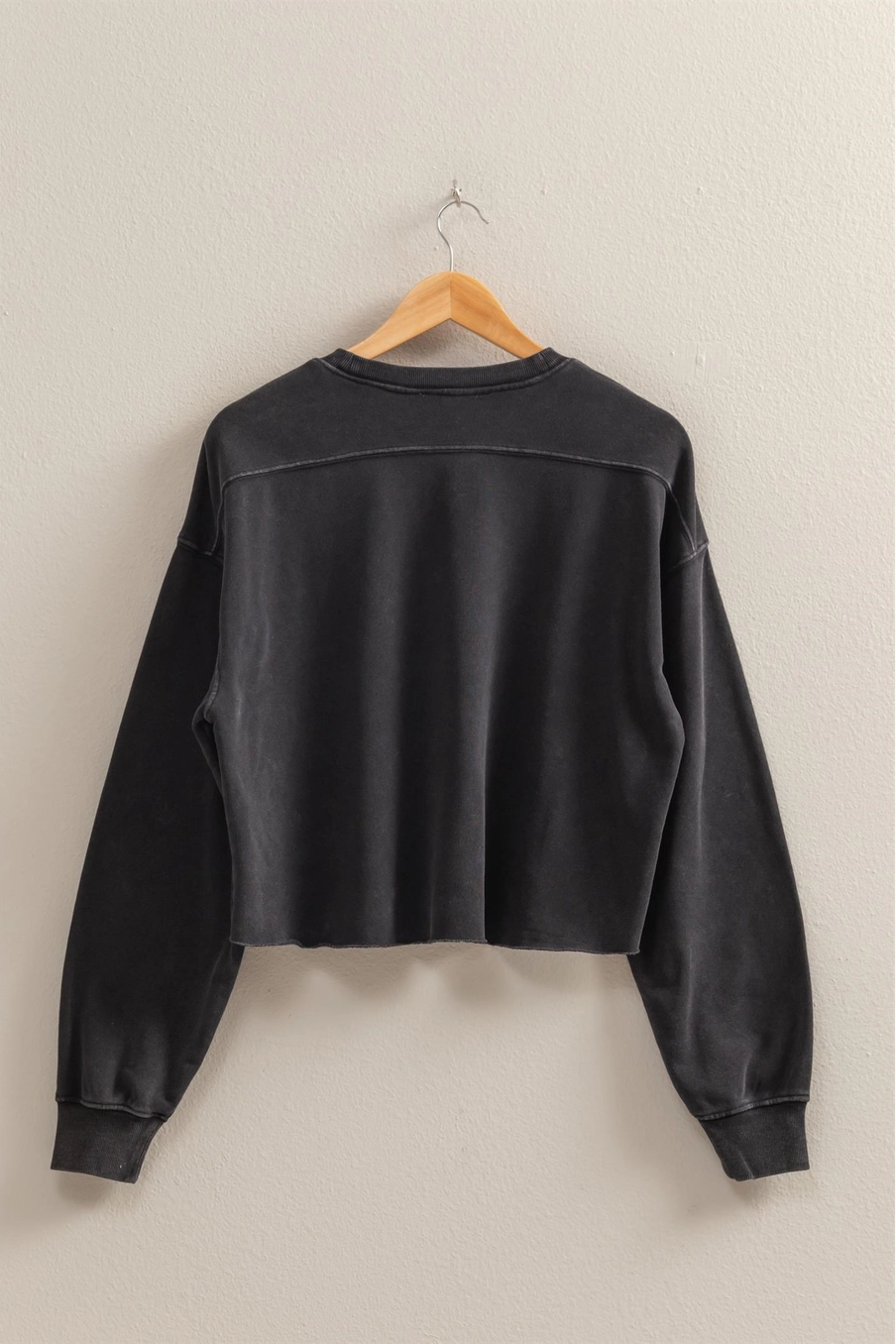 Black sweatshirt on a wooden hanger against a beige background